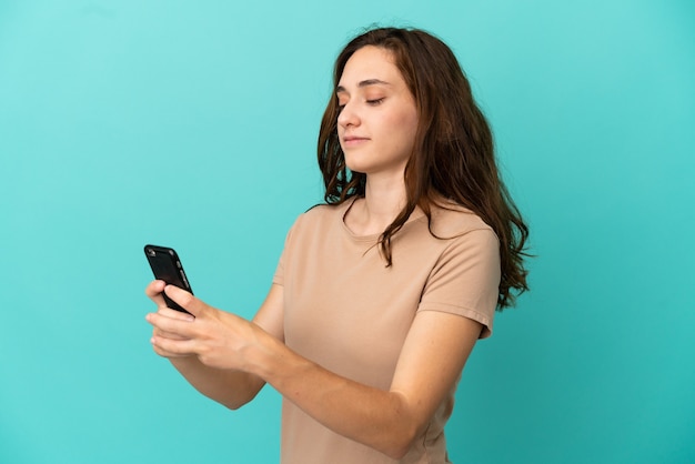 Giovane donna caucasica isolata su sfondo blu che invia un messaggio o un'e-mail con il cellulare