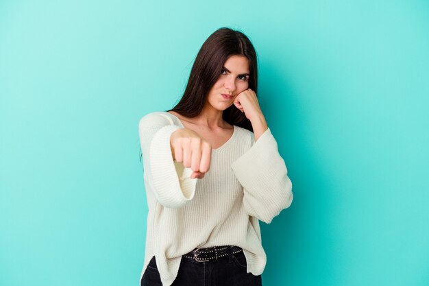 Giovane donna caucasica isolata su sfondo blu che lancia un pugno, rabbia, combattimento a causa di una discussione, boxe.