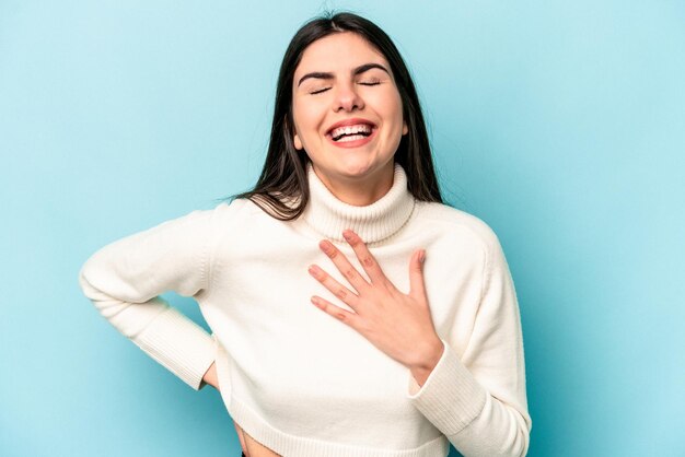 Giovane donna caucasica isolata su sfondo blu che ride tenendo le mani sul concetto di felicità del cuore