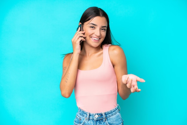 Giovane donna caucasica isolata su sfondo blu che tiene una conversazione con il telefono cellulare con qualcuno