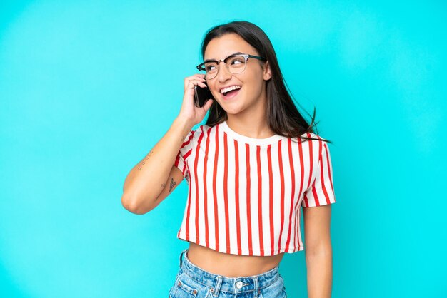 Giovane donna caucasica isolata su sfondo blu che tiene una conversazione con il telefono cellulare