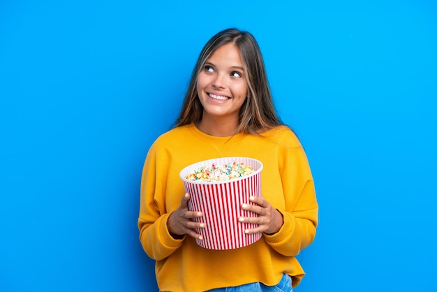 Giovane donna caucasica isolata su sfondo blu con in mano un grande secchio di popcorn