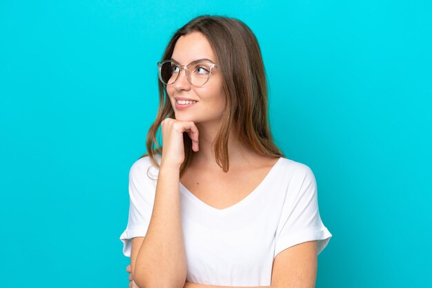 Giovane donna caucasica isolata su sfondo blu Con occhiali e pensare mentre alzando lo sguardo
