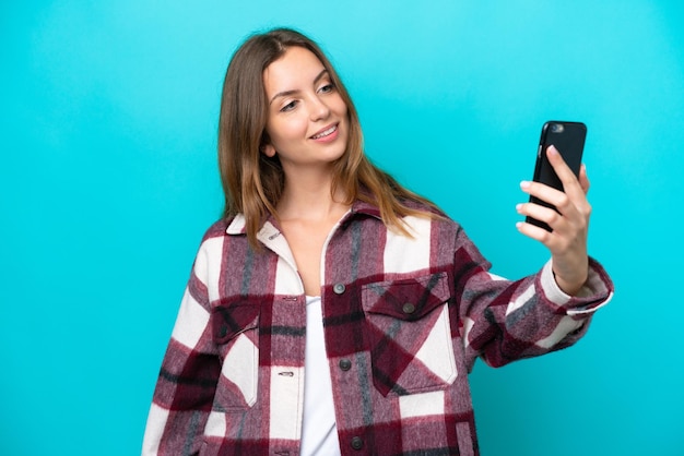 Giovane donna caucasica isolata su sfondo blu facendo un selfie