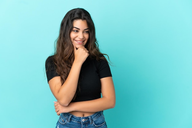 Giovane donna caucasica isolata su sfondo blu guardando di lato e sorridente