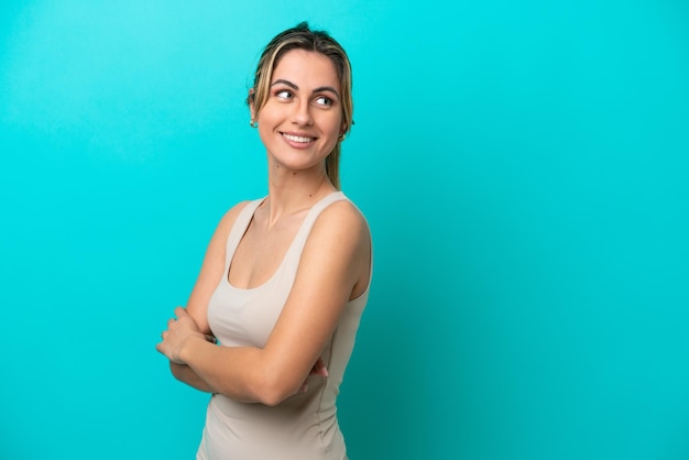 Giovane donna caucasica isolata su sfondo blu guardando di lato e sorridente