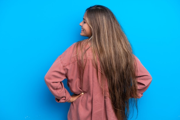 Giovane donna caucasica isolata su sfondo blu in posizione posteriore e guardando di lato