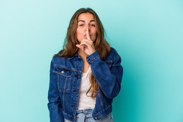 Giovane donna caucasica isolata su sfondo blu mantenendo un segreto o chiedendo silenzio.