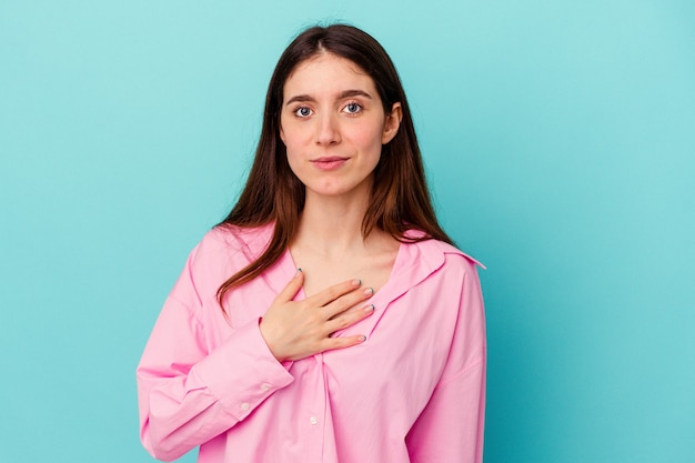 Giovane donna caucasica isolata su sfondo blu prestando giuramento, mettendo la mano sul petto.