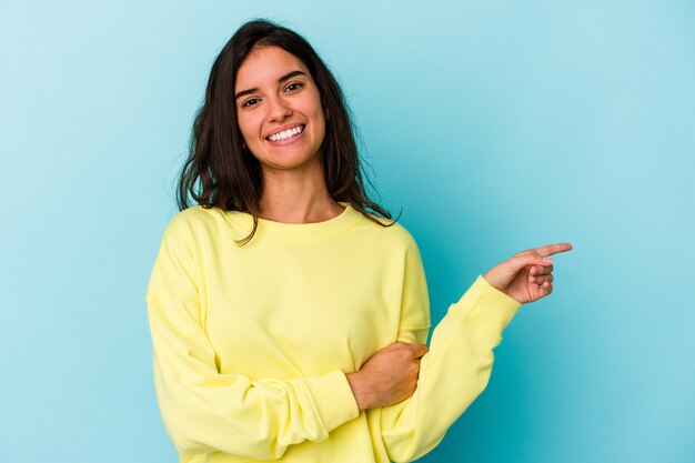 Giovane donna caucasica isolata su sfondo blu sorridente allegramente puntando con l'indice lontano.