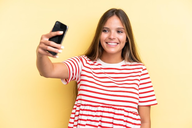 Giovane donna caucasica isolata su sfondo giallo che fa un selfie con il cellulare