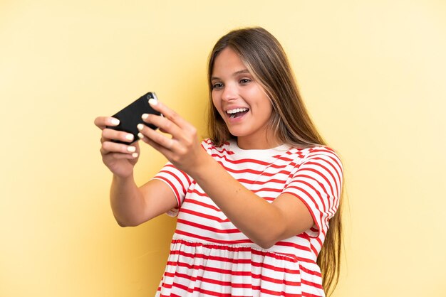 Giovane donna caucasica isolata su sfondo giallo che gioca con il cellulare