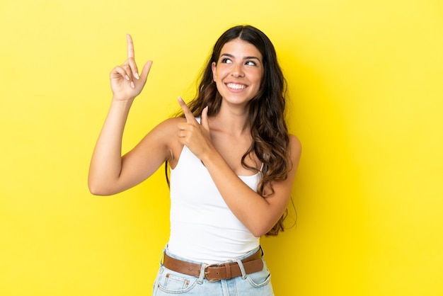 Giovane donna caucasica isolata su sfondo giallo che indica con il dito indice una grande idea