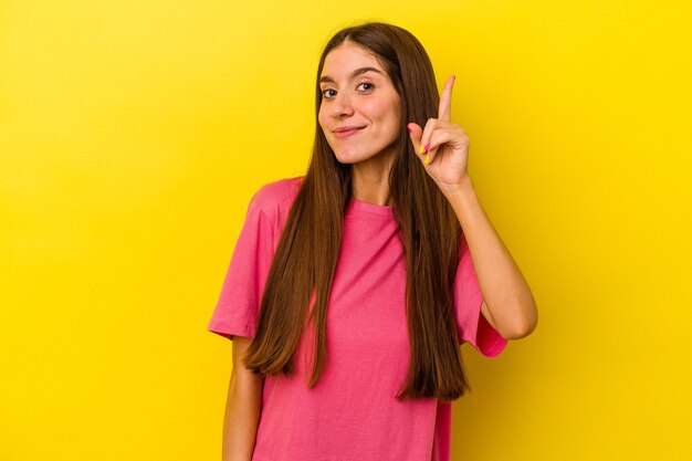 Giovane donna caucasica isolata su sfondo giallo che mostra il numero uno con il dito.