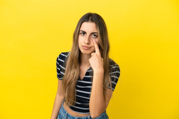 Giovane donna caucasica isolata su sfondo giallo che mostra qualcosa
