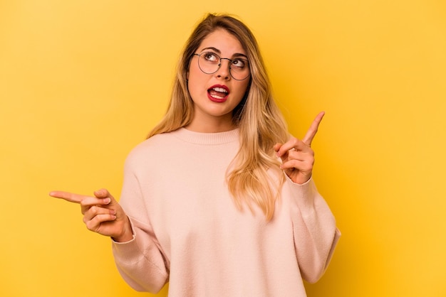 Giovane donna caucasica isolata su sfondo giallo che punta a diversi spazi di copia scegliendone uno che mostra con il dito