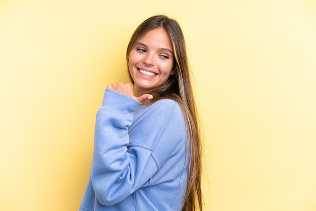 Giovane donna caucasica isolata su sfondo giallo che punta al lato per presentare un prodotto