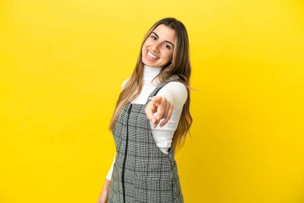 Giovane donna caucasica isolata su sfondo giallo che punta davanti con espressione felice