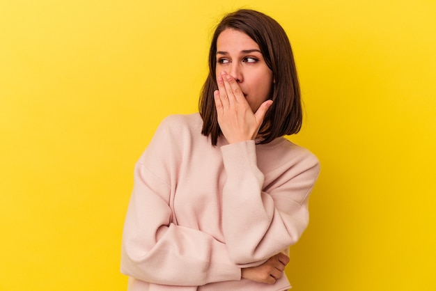 Giovane donna caucasica isolata su sfondo giallo che sbadiglia mostrando un gesto stanco che copre la bocca con la mano.