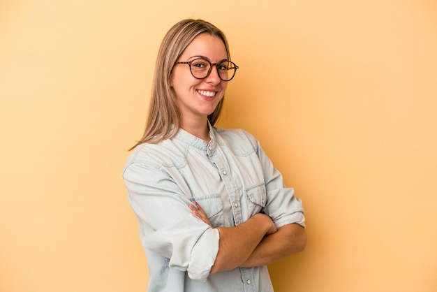 Giovane donna caucasica isolata su sfondo giallo che si sente sicura, incrociando le braccia con determinazione.