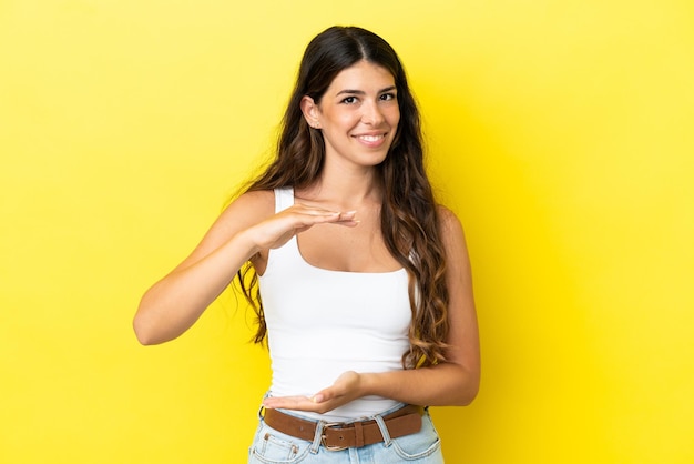 Giovane donna caucasica isolata su sfondo giallo che tiene copyspace immaginario sul palmo per inserire un annuncio