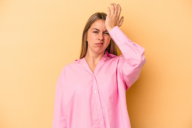 Giovane donna caucasica isolata su sfondo giallo dimenticando qualcosa, schiaffeggiando la fronte con il palmo e chiudendo gli occhi.