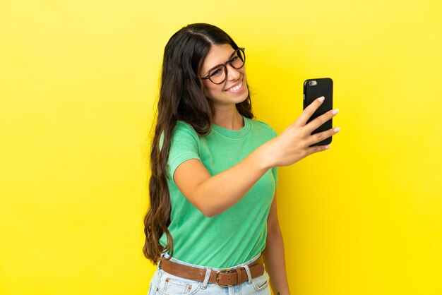 Giovane donna caucasica isolata su sfondo giallo facendo un selfie