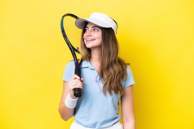 Giovane donna caucasica isolata su sfondo giallo giocando a tennis e alzando lo sguardo