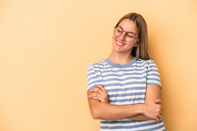 Giovane donna caucasica isolata su sfondo giallo sorridente fiducioso con le braccia incrociate.