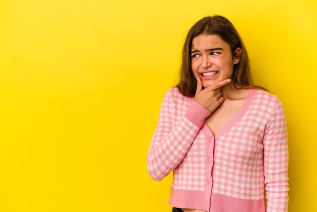 Giovane donna caucasica isolata su sfondo giallo toccando la parte posteriore della testa, pensando e facendo una scelta.