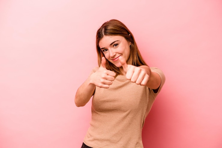 Foto giovane donna caucasica isolata su sfondo rosa alzando entrambi i pollici sorridenti e fiduciosi