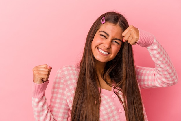 Giovane donna caucasica isolata su sfondo rosa alzando il pugno dopo una vittoria, concetto vincitore.