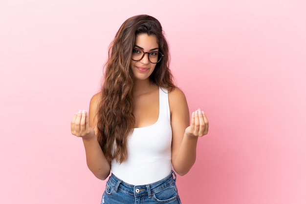 Giovane donna caucasica isolata su sfondo rosa che fa un gesto di denaro ma è rovinata