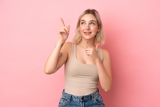 Giovane donna caucasica isolata su sfondo rosa che indica con il dito indice una grande idea