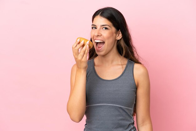 Giovane donna caucasica isolata su sfondo rosa che mangia una ciambella