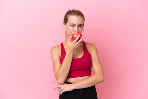 Giovane donna caucasica isolata su sfondo rosa che mangia una mela