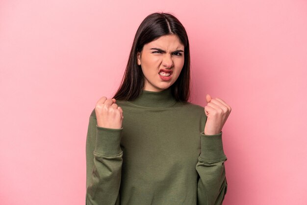 Giovane donna caucasica isolata su sfondo rosa che mostra il pugno all'espressione facciale aggressiva della fotocamera