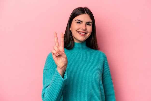 Giovane donna caucasica isolata su sfondo rosa che mostra il segno di vittoria e sorride ampiamente