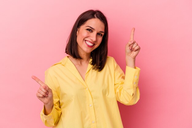 Giovane donna caucasica isolata su sfondo rosa che punta a diversi spazi di copia, scegliendone uno, mostrando con il dito.