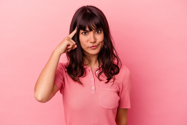 Giovane donna caucasica isolata su sfondo rosa che punta il tempio con il dito, pensando, concentrata su un compito.