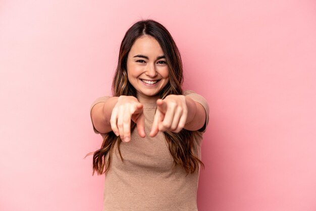 Giovane donna caucasica isolata su sfondo rosa che punta in avanti con le dita