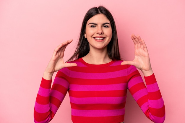 Giovane donna caucasica isolata su sfondo rosa che tiene qualcosa con le palme che offrono alla fotocamera