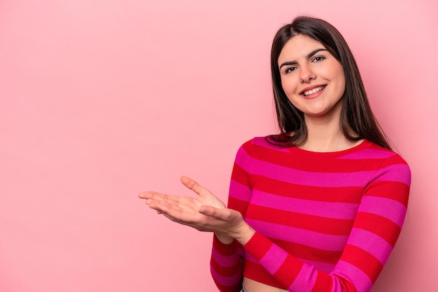 Giovane donna caucasica isolata su sfondo rosa che tiene uno spazio di copia su un palmo