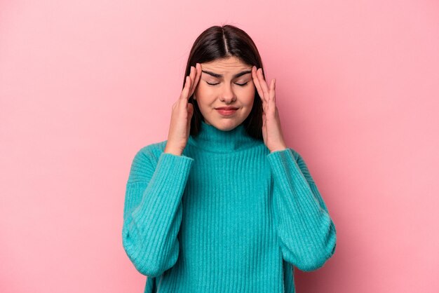 Giovane donna caucasica isolata su sfondo rosa che tocca le tempie e ha mal di testa