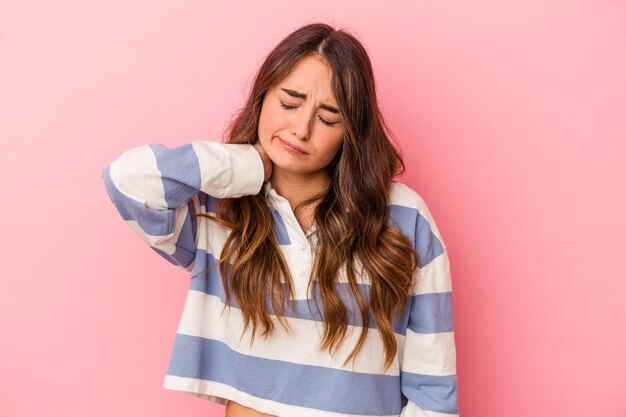 Giovane donna caucasica isolata su sfondo rosa con dolore al collo dovuto allo stress, massaggiandolo e toccandolo con la mano.