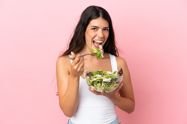 Giovane donna caucasica isolata su sfondo rosa con in mano una ciotola di insalata con espressione felice