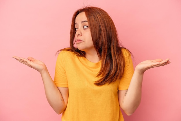 Giovane donna caucasica isolata su sfondo rosa confusa e dubbiosa alzando le spalle per tenere uno spazio di copia.