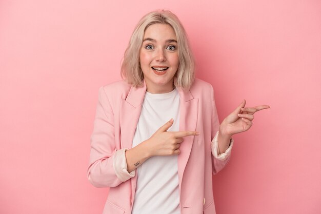 Giovane donna caucasica isolata su sfondo rosa eccitato indicando con l'indice lontano.