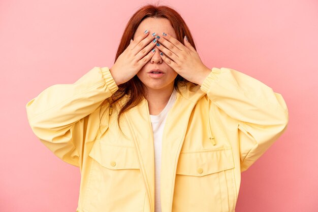 Giovane donna caucasica isolata su sfondo rosa impaurita che copre gli occhi con le mani.