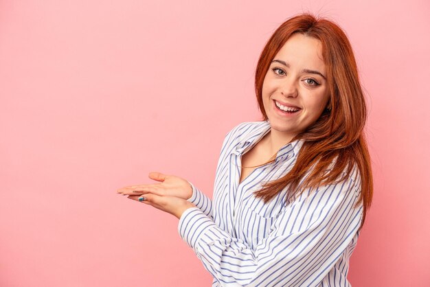 Giovane donna caucasica isolata su sfondo rosa in possesso di uno spazio di copia su un palmo.